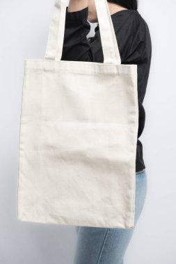 Siyah tişörtlü ve kot pantolonlu biri tarafından tutulan sade beyaz bir çanta.