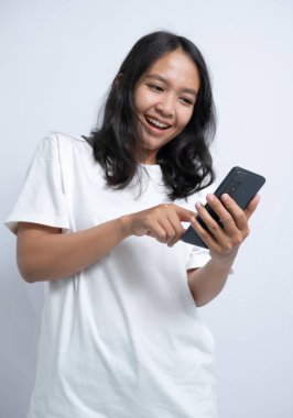 Genç bir kadın gülümsüyor ve telefonuna bakıyor. Sağ eli telefonu tutuyor ve sol eli ekranla etkileşimde.