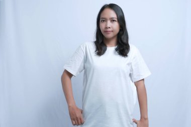 Beyaz tişörtlü genç bir kadın, elleri kalçasında güvenle ayakta duruyor.