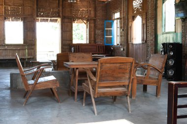 Ahşap sandalyeler ahşap bir masanın etrafında tuğla duvarlı ve büyük ahşap pencereli bir odada otururlar.