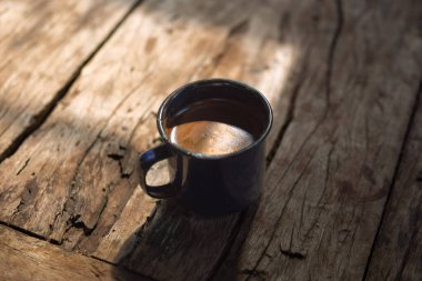 Bir fincan kahve, pencerenin gölgesi olan ahşap bir masada oturuyor.