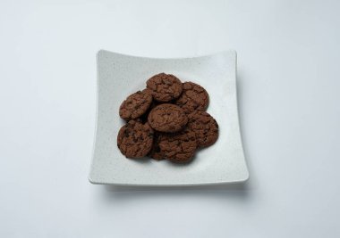 Beyaz bir yüzeyde duran bir tabak çikolata parçalı kurabiye.