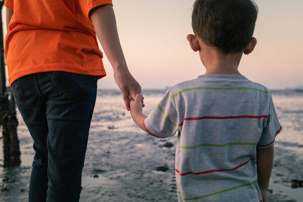 Мать держит сына за руку, а мальчик смотрит на пляж.