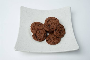 Çikolata parçalı kurabiyeler beyaz tabakta yığılmış.