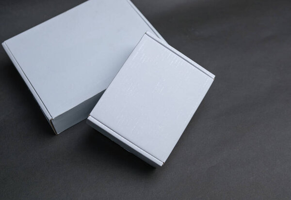 Две белые коробки сидят рядом друг с другом. Большая коробка лежит ровно, в то время как меньшая коробка частично на ней.