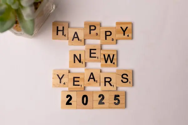 Tahta karolar mutlu yeni yıl 2025 yazılıyor beyaz masada, üst görünümde.