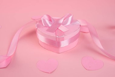 Pembe kurdeleli kalp şeklinde bir hediye kutusu pembe bir yüzeyde duruyor. Sevgililer Günü konsepti