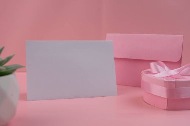 Pembe bir zarf ve pembe kurdeleli kalp şeklinde bir hediye kutusunun yanında boş bir kart duruyor. model kart tasarımı