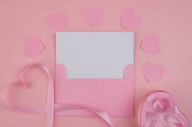 İçinde pembe kalpler, kalp şeklinde kurdele ve hediye olan boş bir kart olan pembe bir zarf.