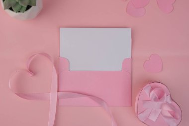 Kalp şeklinde bir hediye kutusunun yanında pembe kurdeleli boş bir kartın bulunduğu pembe bir zarf. davet modelleme tasarımı