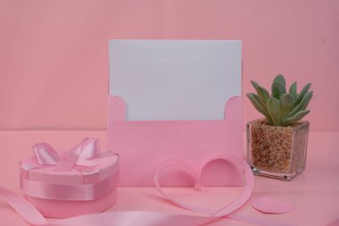 İçinde boş bir kart olan pembe bir zarf, içinde kurdele olan pembe bir hediye kutusunun yanında duruyor. davet düzenleme konsepti
