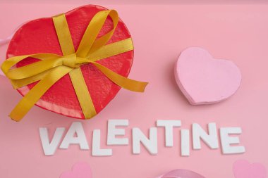 Altın kurdeleli kırmızı kalp şeklinde bir kutu VALENTINE sözcüğünün yanında oturur.