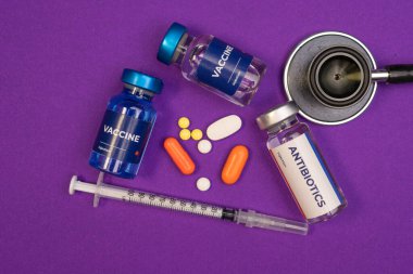 İki aşı şişesi bir antibiyotik şişesi bir şırınga hapı ve bir steteskop mor bir yüzeyde yatıyor. Sağlık ve Tıp Konsepti