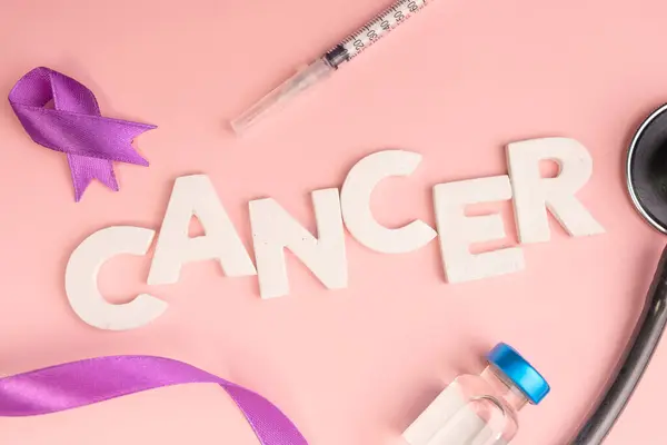 Kanser kelimesi mor bir kurdele, şırınga ve steteskop ile çevrili beyaz harflerle hecelenir.