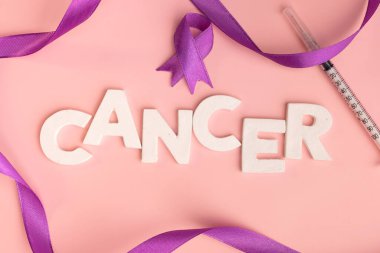 White letters spelling out the word cancer lie on a pink surface next to purple ribbons and a syringe. World cancer day concept clipart