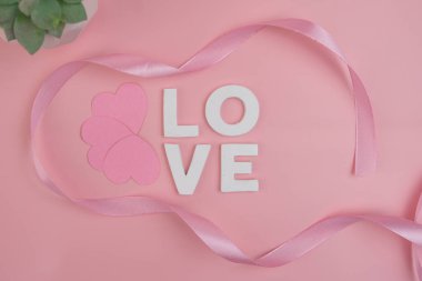 Aşk sözcüğünü çevreleyen pembe kalpler ve kurdele
