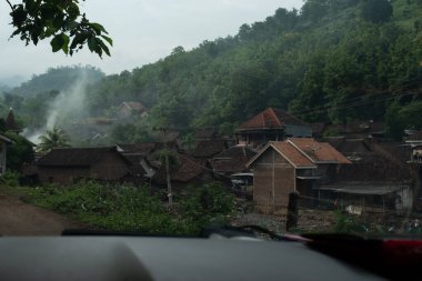 İçinden duman yükselen yemyeşil bir yamaçta yuva yapmış bir köy.