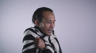 Solgun yüzlü bir adam evinde üşüyor battaniyesini giyiyor, grip oluyor, evde titriyor..