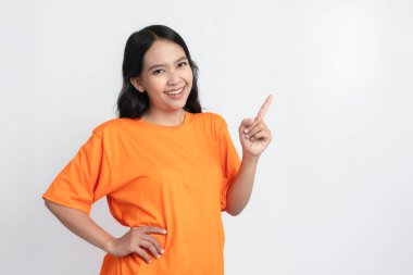 Turuncu tişört giyip gülümseyen ve sağını gösteren bir kadın.