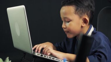 Bir çocuk siyah bir masada internette sörf yapmak için dizüstü bilgisayarında klavye kullanıyor. teknoloji eğitimi kavramı