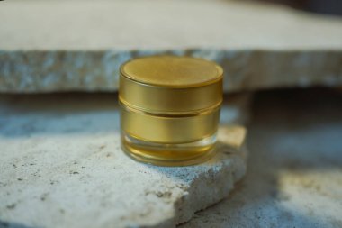 Altın krema kavanozu mermer taşların üzerinde duruyor. Güzellik konsepti