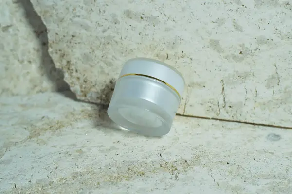 Bir mermer taşın üzerinde duran beyaz krema kavanozu.