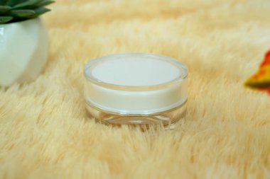 Sarı bir kürkün üzerinde duran beyaz krema kavanozuna yaklaş. ürün modelleme görüntüsü için kullan