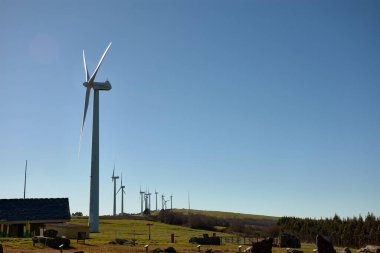 Güneşli bir dağ manzarasında rüzgar türbinleri. Dağ Rüzgâr Çiftliği 'nin kıvrımlı yolu. Yeşil enerji üretimi. Rüzgâr tarlası ekolojik alanı. Yenilenebilir enerji konsepti, yeşil enerji üretimi. Enerji endüstrisi.