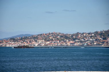 Playa America kıyılarında küçük evler, turkuaz mavi bir deniz ve Nigran, Pontevedra, İspanya 'da açık bir gökyüzü.