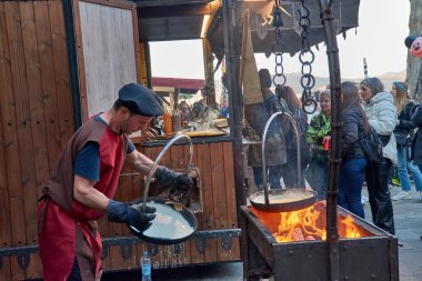 Baiona, Pontevedra, Galiçya, İspanya; Mart 04.2023; Ortaçağ aşçısı, insanların özenli bakışları önünde ateşten gözleme yapar