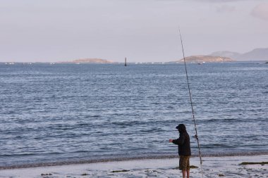 BAIONA, PONTEVEDRA, SPAIN; Temmuz 07.2021: Un pescador en la Playa de la ladeira en baiona esperando para ver si pican los peces