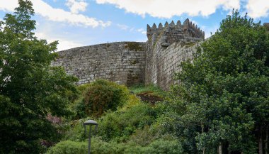 Portekiz 'deki Castro Laboreiro Kalesi' nin dış duvarı. Bulutlu bir günde ağaçlar ve yeşilimsi bir bitki örtüsü. Aşağıdan görüntüle