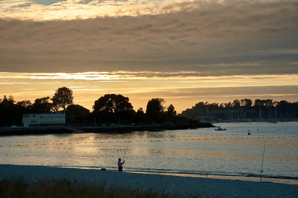 stock image A beautiful sunset paints the sky over Ladeira Beach in Sabaris, as a solitary fisherman works on the shore. The golden light of the setting sun reflects on the water, creating an atmosphere of peace and contemplation on this picturesque Galician bea