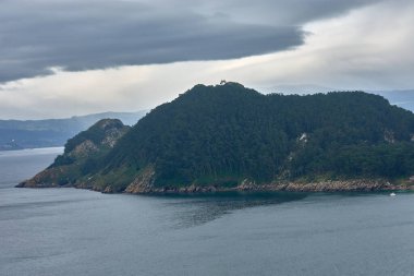 İspanya, Galiçya açıklarındaki Cies Adaları 'nın etkileyici güzelliğinin resmi. Görüntü, Atlantik Okyanusu 'nun turkuaz sularının yavaşça kayalık sahili kapladığı muhteşem bir uçurumu gösteriyor.