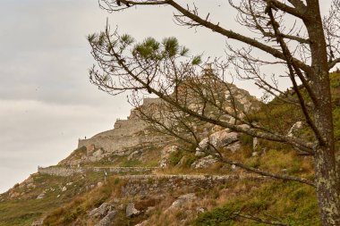 Düşük bir açıdan çekilen bu çarpıcı panoramik fotoğraf İspanya 'nın Galiçya kentindeki Cies Adaları' ndaki ikonik deniz fenerini yakalar. Görüntülerde deniz feneri berrak mavi gökyüzüne karşı dimdik ayakta duruyor. Etrafı engebeli doğal güzelliklerle çevrili. 