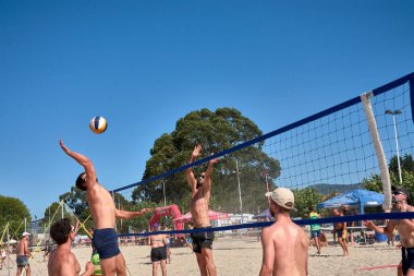 Baiona 'da düzenlenen 3x3 Ladeira Plaj Voleybol Turnuvası' nda oyuncular kollarını kaldırıp ağda güçlü bir blok oluşturdular. Sahne, plaj voleybolunda gerekli rekabet ruhunu ve takım çalışmasını yakalıyor..