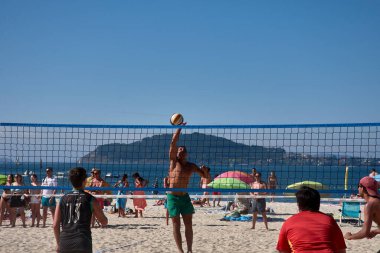Baiona 'da düzenlenen 3x3 Ladeira Plaj Voleybol Turnuvası' nda oyuncular kollarını kaldırıp ağda güçlü bir blok oluşturdular. Sahne, plaj voleybolunda gerekli rekabet ruhunu ve takım çalışmasını yakalıyor..
