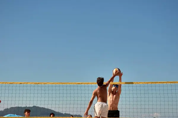 stock image In an intense moment during the 3x3 Ladeira Beach Volleyball Tournament in Baiona, players leap with arms raised, executing a powerful block at the net. The scene captures the competitive spirit and teamwork essential in beach volleyball.