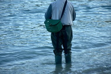 the traditional attire of a fisherman wading in the water, equipped with sturdy boots and a basket for holding the catch.  clipart