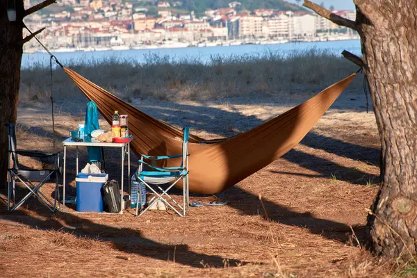 stock image illegal camping site, featuring a hammock strung between two trees and a table nearby with food items. The setup is nestled within a forested area, creating an intimate but unauthorized camp