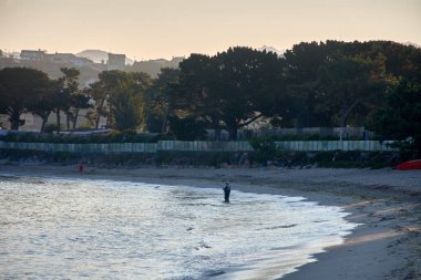 Şafak vakti Baiona 'daki Playa de la Ladeira' nın nefes kesici güzelliği. Güneş doğarken, altın ışığı kumlu sahili ve sakin suları yıkayarak sakin ve huzurlu bir atmosfer yaratıyor.