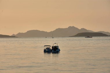 Güneş Baiona Körfezi 'nde batarken pruvaları görkemli Cies Adaları' na dönük tekneler sakin ve güzel bir manzara yaratıyor. Günbatımının ılık, altın rengi sakin sulardan yansıyarak deniz yolculuğunun güzelliğini arttırır.
