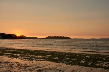 Extraordinary sunset at Ladeira Beach in Bayona, where vibrant orange hues paint the sky, creating a mesmerizing and unforgettable scene. The sun dips below the horizon, casting a warm and radiant glow across the calm waters and sandy shores.  clipart