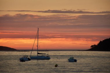 A red-hued sunset over Playa Amrica in Nigrn, Spain, with the silhouette of Las Estelas islands in the background. The sky is painted in deep shades of red, orange, and pink as the sun dips below the horizon, casting a warm glow across the water clipart