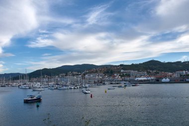 İspanya, Pontevedra, Bayona 'daki Barbeira Sahili' nden sakin bir sahne. Körfezin sakin suları, yumuşak, ince bulutlu, berrak mavi bir gökyüzünün altında barış içinde demirlemiş yelkenli ve küçük yatlarla doludur..