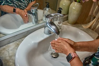 Günlük hijyen uygulaması: akan suyun altında ellerini yıkamak. Modern bir banyo lavabosunda ellerini yıkayan bir kadın..