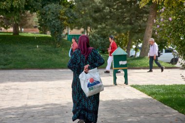 Taşkent, Özbekistan; Eylül, 16. 2024: Özbekistan 'ın başkenti Taşkent' te hareketli bir pazarda yürürken çarpıcı sarı başörtüsü takan Müslüman bir kadın. 