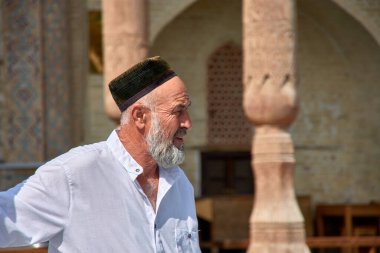 Buhara, Özbekistan; Eylül 19.2024: Özbekistan 'ın Buhara kentinde geleneksel Tyubeteika şapkasını takan beyazlar içinde Özbek bir adamın yakın çekimi.