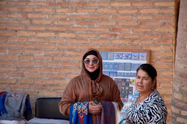 Kihva, Özbekistan; Eylül 21, 2024: Kahverengi kıyafet giymiş şık bir Müslüman kadın ve büyük güneş gözlükleriyle tamamlanmış aynı tesettür. Özbekistan, Khiva sokaklarında yürüyor.