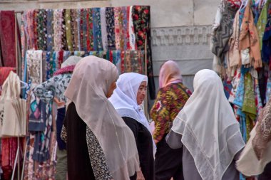 Semerkant, Özbekistan; 18 Eylül 2024: Geleneksel peçeler giymiş bir grup Özbek kadın, canlı ipek kumaş dükkanlarının önünden geçen Semerkant 'ın hareketli sokaklarında yürüyor. 